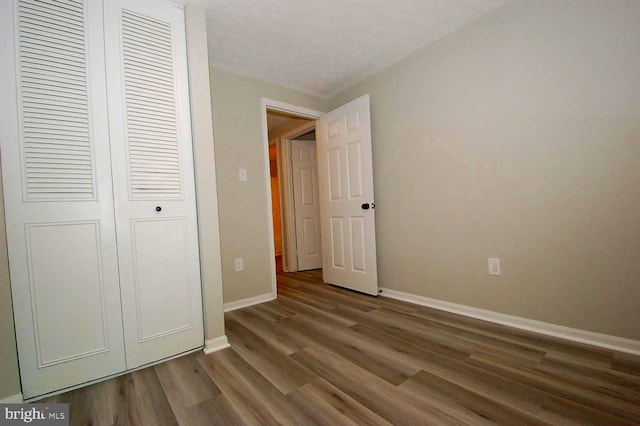 unfurnished bedroom with baseboards, a textured ceiling, wood finished floors, and a closet