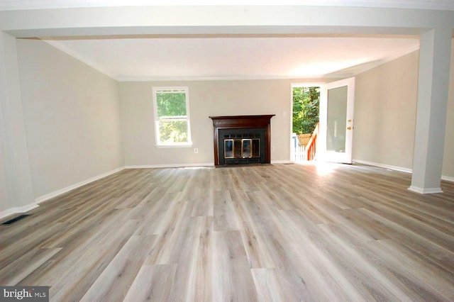 unfurnished living room with light wood finished floors, a glass covered fireplace, baseboards, visible vents, and ornamental molding