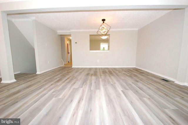 spare room featuring visible vents, light wood finished floors, crown molding, and baseboards