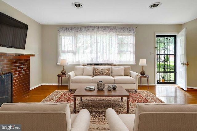 living area featuring a fireplace, baseboards, visible vents, and wood finished floors