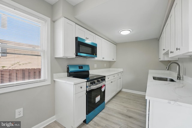 kitchen featuring baseboards, white cabinets, a sink, a wealth of natural light, and stainless steel appliances