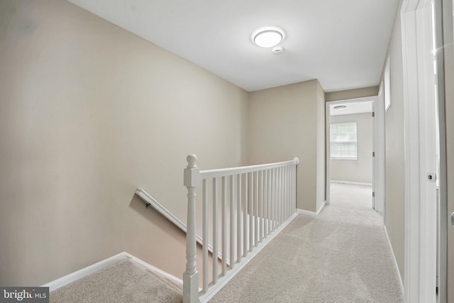 corridor featuring baseboards, an upstairs landing, and carpet