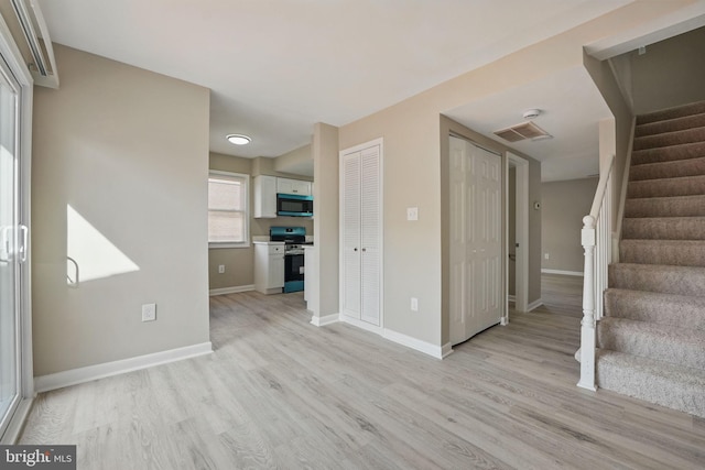 unfurnished living room with baseboards, visible vents, light wood finished floors, and stairs