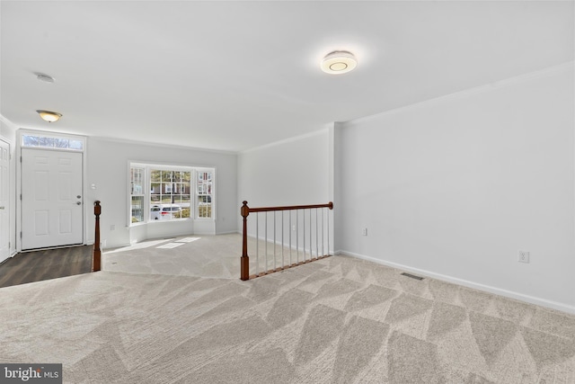 carpeted entryway featuring crown molding, baseboards, and visible vents