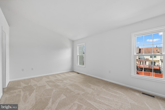 empty room featuring vaulted ceiling, baseboards, light colored carpet, and visible vents