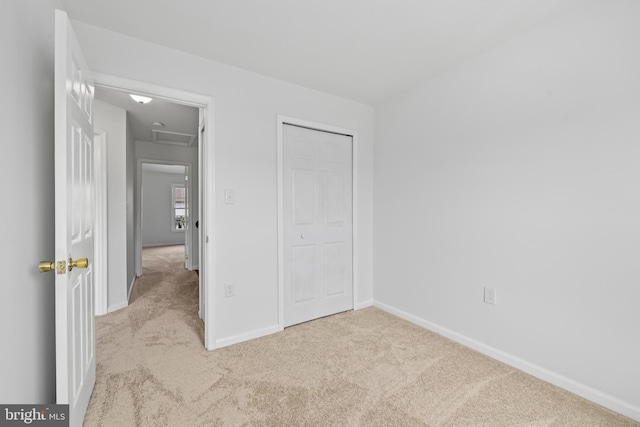unfurnished bedroom with baseboards, attic access, carpet, and a closet