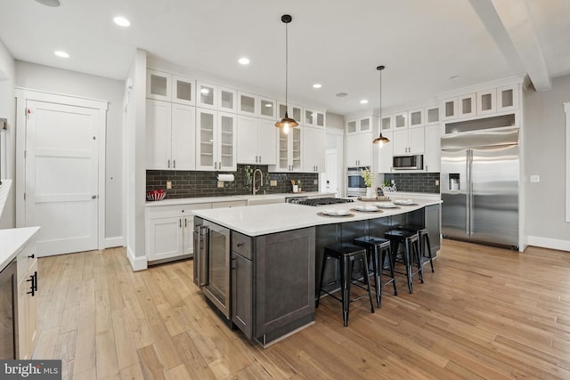 kitchen with a kitchen island, appliances with stainless steel finishes, tasteful backsplash, light wood-type flooring, and light countertops