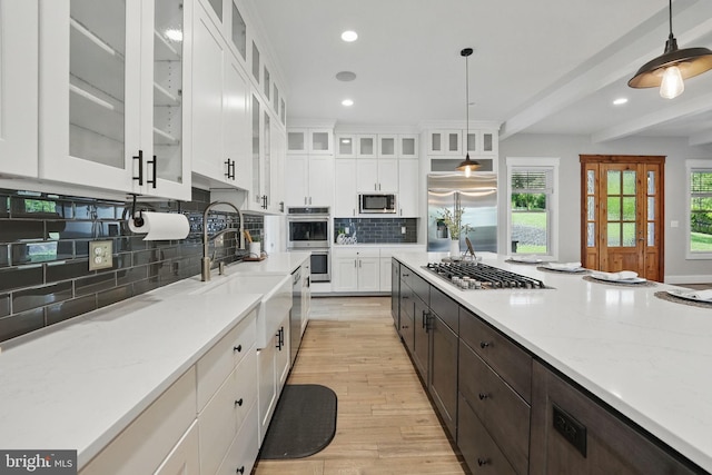 kitchen featuring tasteful backsplash, a sink, white cabinets, built in appliances, and light wood-style flooring