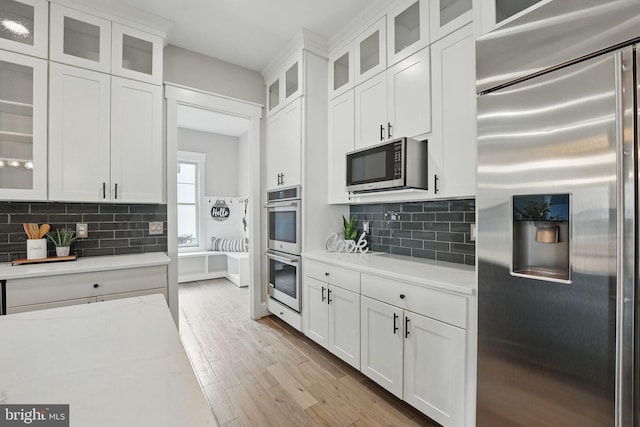 kitchen with stainless steel appliances, white cabinetry, light wood-type flooring, backsplash, and glass insert cabinets