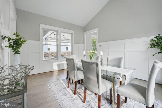 dining area featuring wood finished floors, a decorative wall, high vaulted ceiling, and a wainscoted wall
