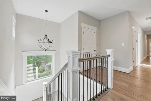 corridor with visible vents, light wood-type flooring, baseboards, an upstairs landing, and an inviting chandelier