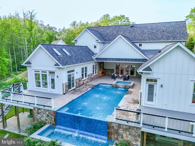 back of house featuring stone siding, a wooden deck, board and batten siding, an outdoor pool, and an in ground hot tub