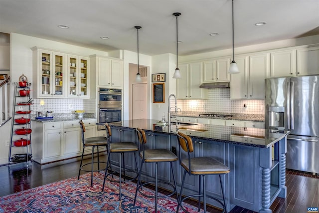 kitchen featuring a sink, stainless steel appliances, tasteful backsplash, under cabinet range hood, and dark wood-type flooring