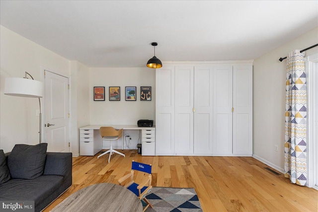 office with baseboards, visible vents, built in desk, and light wood finished floors