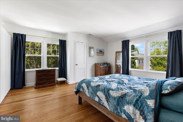 bedroom featuring visible vents, light wood finished floors, vaulted ceiling, and multiple windows