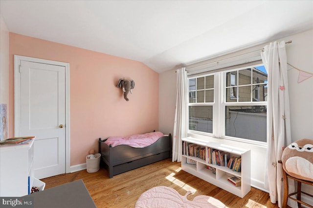 bedroom featuring baseboards, wood finished floors, and lofted ceiling