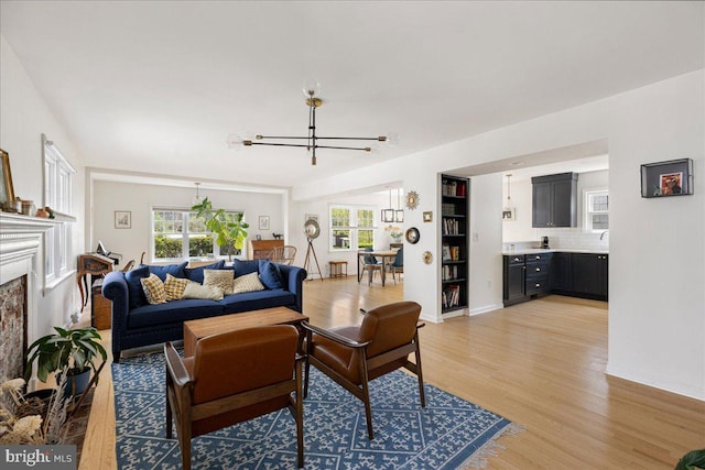 living room featuring baseboards, a chandelier, light wood finished floors, and a high end fireplace