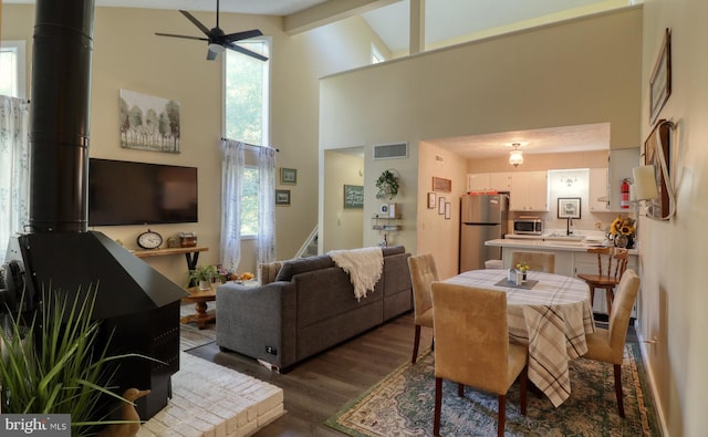 living room featuring visible vents, a wood stove, ceiling fan, a high ceiling, and dark wood-style floors
