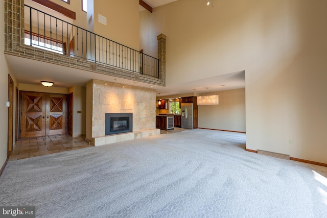 unfurnished living room with carpet flooring, a fireplace, baseboards, a towering ceiling, and visible vents