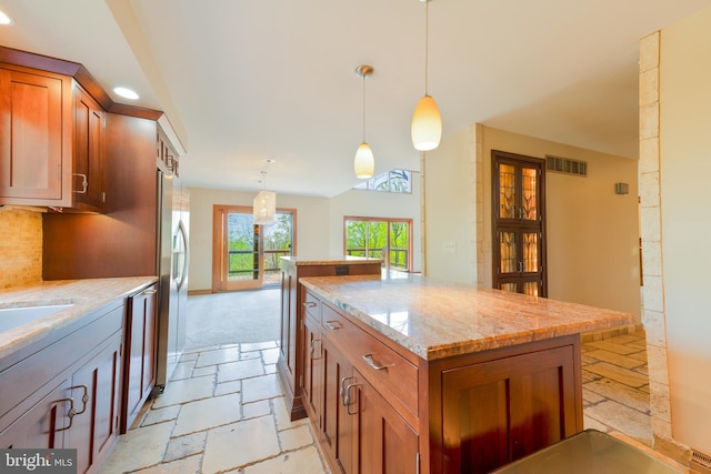 kitchen featuring brown cabinetry, a kitchen island, visible vents, light stone countertops, and stone tile flooring