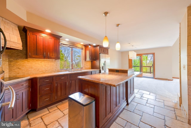 kitchen featuring stone tile floors, decorative backsplash, stainless steel fridge, a center island, and a sink