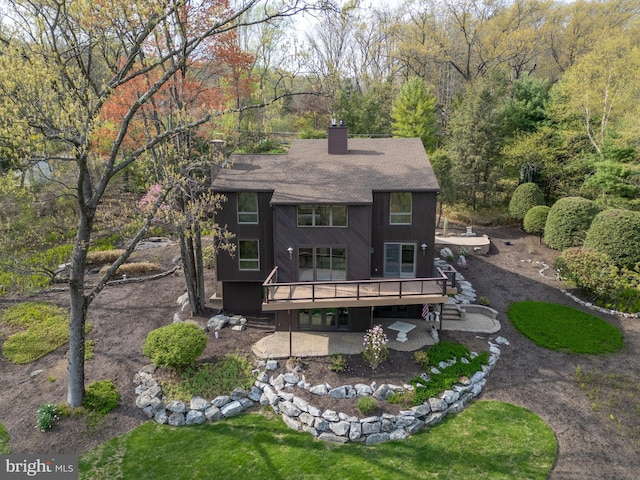 back of house featuring a shingled roof, a wooden deck, stairway, a chimney, and a patio