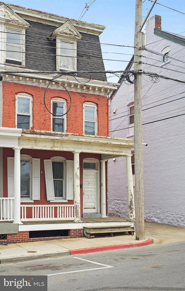 victorian home with covered porch, brick siding, and mansard roof