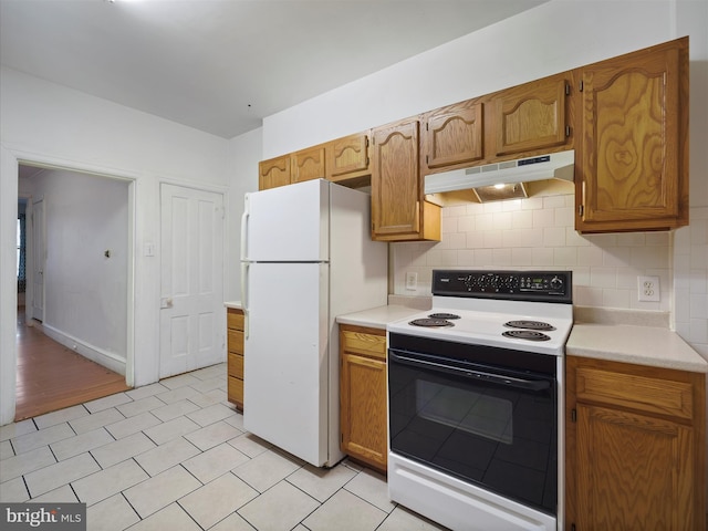 kitchen featuring freestanding refrigerator, under cabinet range hood, decorative backsplash, light countertops, and electric stove