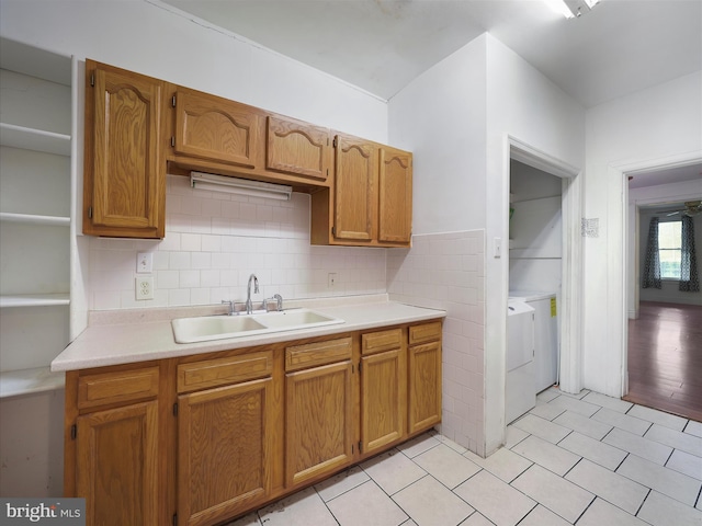 kitchen with a sink, brown cabinetry, light countertops, light tile patterned flooring, and washer / clothes dryer