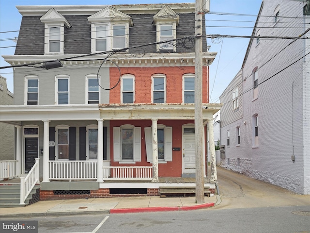 second empire-style home with a porch, a shingled roof, brick siding, and mansard roof