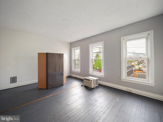 empty room featuring a wall mounted AC, baseboards, dark wood-type flooring, and visible vents