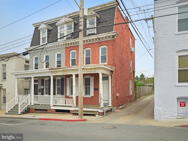 second empire-style home featuring a shingled roof, brick siding, and covered porch
