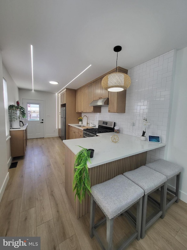 kitchen featuring a sink, light countertops, baseboards, under cabinet range hood, and stainless steel appliances
