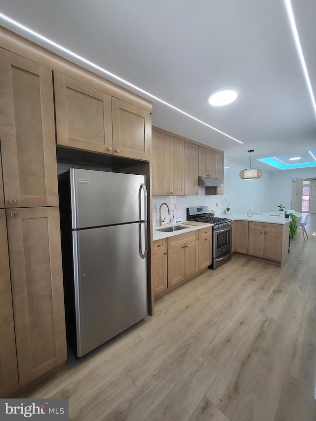 kitchen featuring a sink, a peninsula, under cabinet range hood, light wood-style floors, and stainless steel appliances