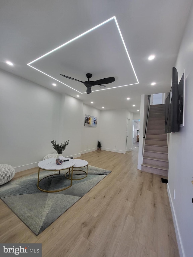 living room featuring light wood-type flooring, a ceiling fan, stairs, and baseboards