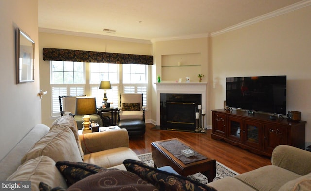 living area with a glass covered fireplace, visible vents, built in features, crown molding, and wood finished floors