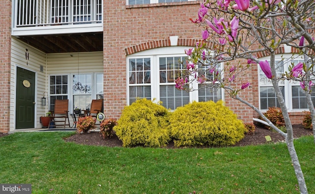 doorway to property featuring a yard, brick siding, and a balcony