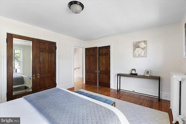 bedroom featuring wood finished floors, radiator heating unit, baseboards, and a closet