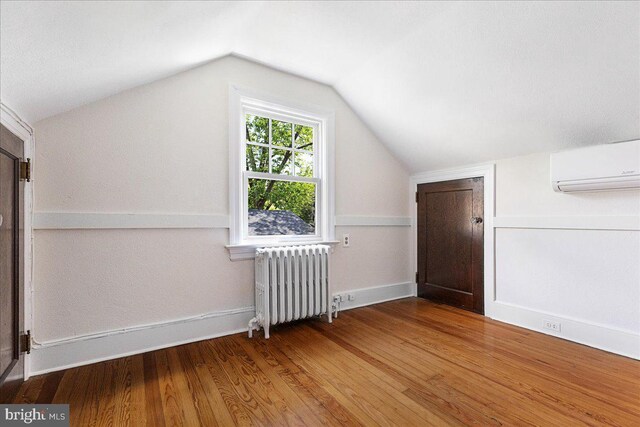 bonus room featuring radiator, a wall unit AC, wood finished floors, vaulted ceiling, and baseboards