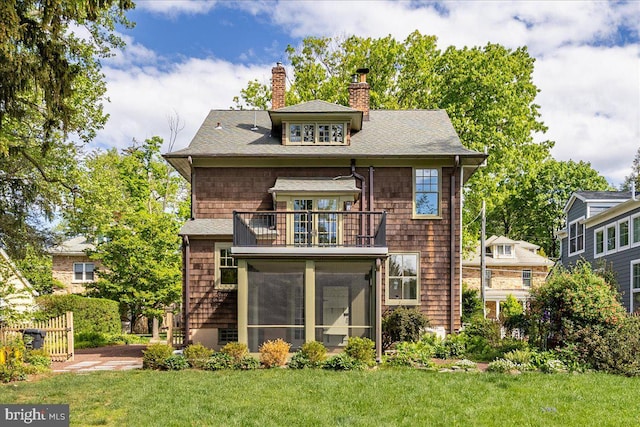 rear view of house featuring a balcony, a chimney, a yard, a sunroom, and a shingled roof