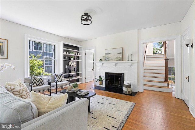 living area with wood finished floors, stairs, a fireplace, and built in shelves