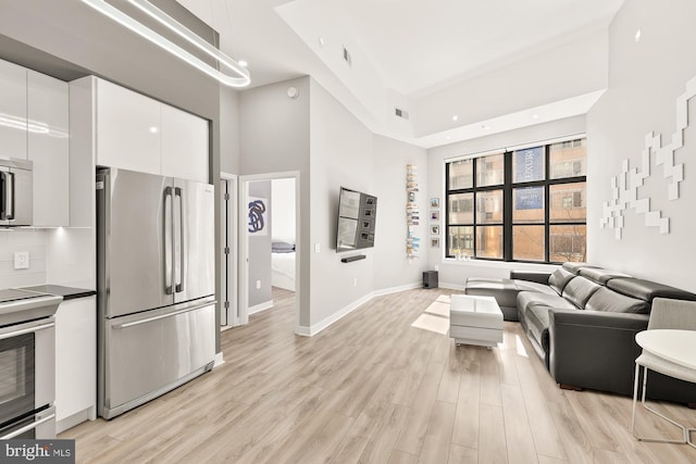 living area with baseboards, visible vents, light wood finished floors, and a towering ceiling