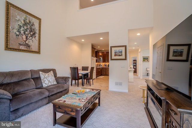 living area with light carpet, recessed lighting, baseboards, a towering ceiling, and visible vents