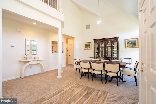 dining space with baseboards, visible vents, wood finished floors, and high vaulted ceiling