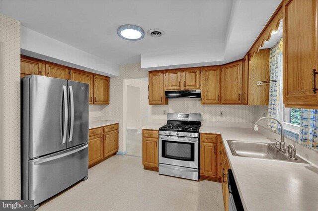 kitchen featuring brown cabinetry, appliances with stainless steel finishes, a sink, light countertops, and under cabinet range hood