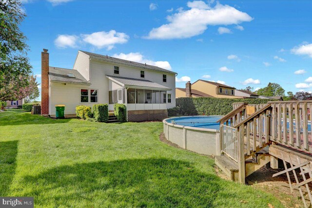 back of house with a chimney, a lawn, a wooden deck, a sunroom, and a fenced in pool