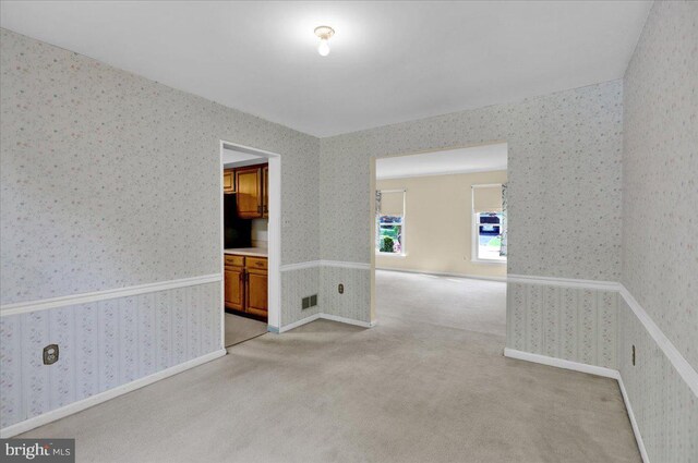 spare room featuring light colored carpet, wallpapered walls, and visible vents