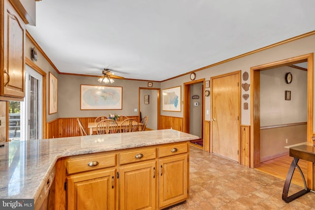 kitchen with wood walls, a wainscoted wall, a peninsula, a ceiling fan, and ornamental molding
