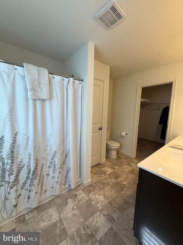 bathroom with toilet, a walk in closet, stone finish floor, visible vents, and baseboards