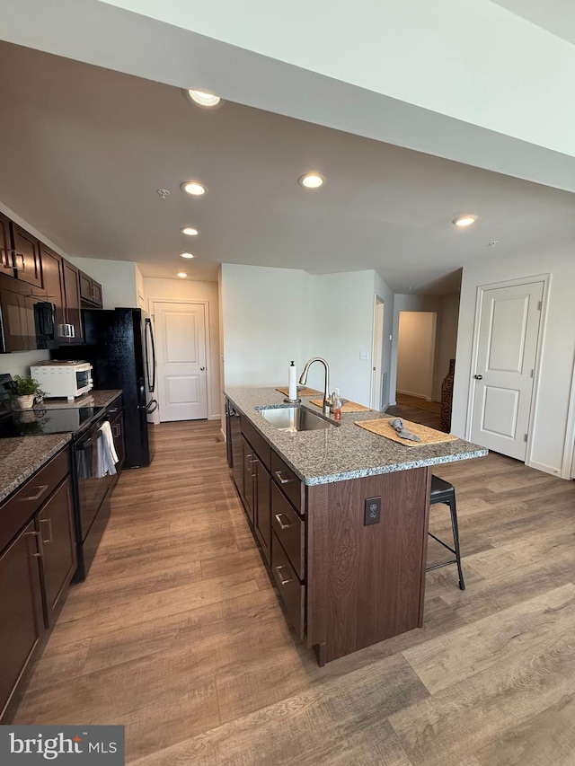 kitchen featuring a breakfast bar area, wood finished floors, black appliances, and a sink